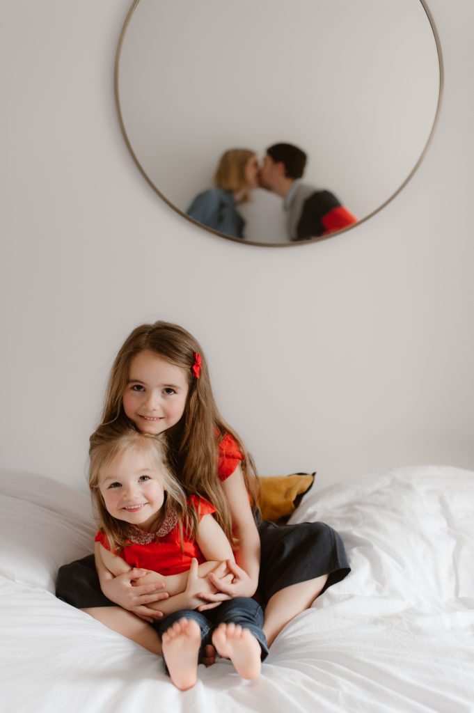 Petites filles sur le lit de leur parents qui s'embrassent en reflet dans le miroir à l'arrière plan